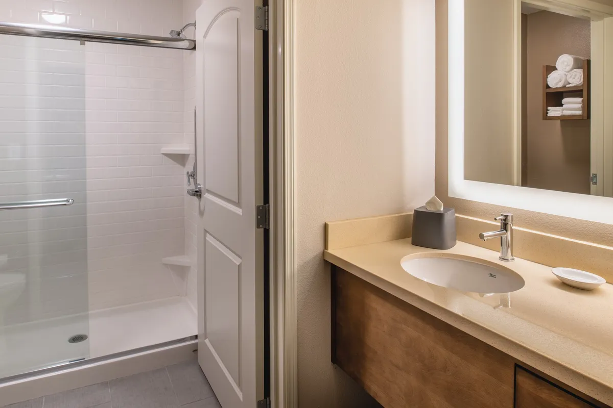A sleek interior space focused on a modern shower stall, sink area, and large mirror. The atmosphere is calming and functional, emphasizing refreshment and self-care after a workout or swim.