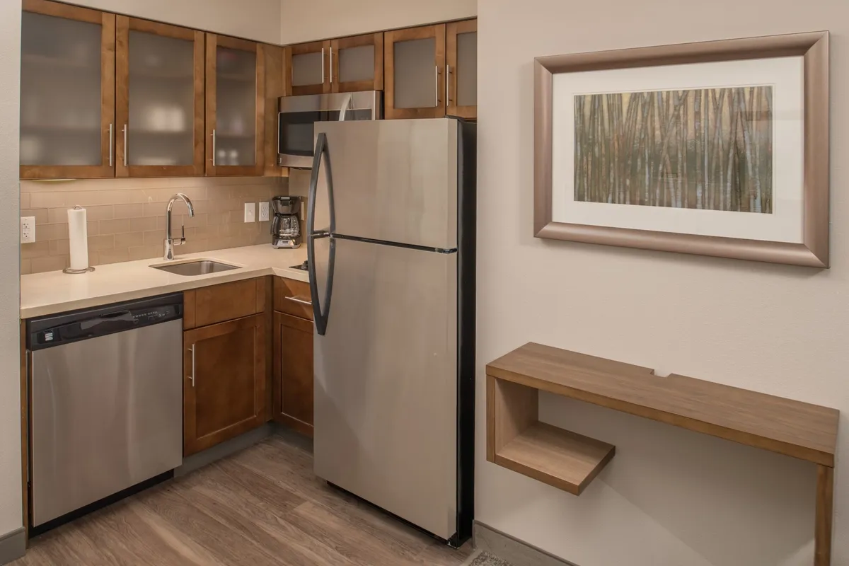 A contemporary kitchen scene with a stainless steel refrigerator and modern cabinetry, set against the backdrop of tasteful wall art. The space is lively and functional—people are seen cooking breakfast together, engaging in casual conversation, and preparing for meals, which highlights the full kitchen amenities.