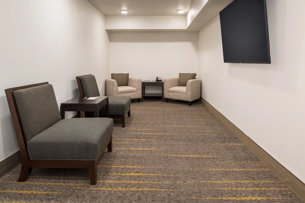 A compact interior scene with a comfortable seating arrangement, a small table, and a television. The mood is relaxed and intimate, ideal for unwinding or enjoying a quiet moment. The decor is modern and understated, aligning with a private, restful retreat.