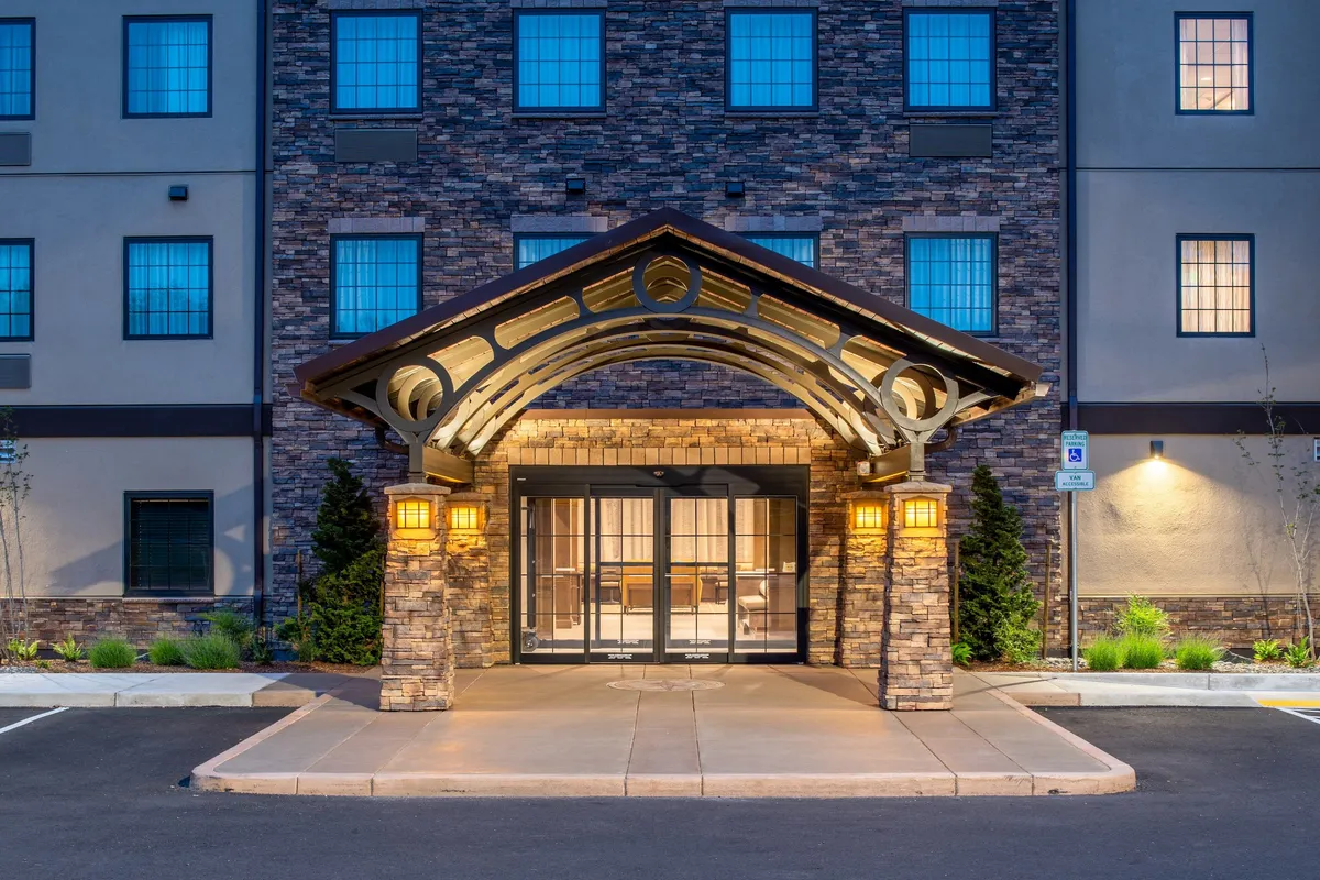 The hotel's grand arched entrance and stone facade are warmly lit, creating an inviting sense of arrival. Guests are seen checking in, greeting each other, and unloading luggage, capturing the excitement of starting a family getaway and the welcoming nature of the accommodation.